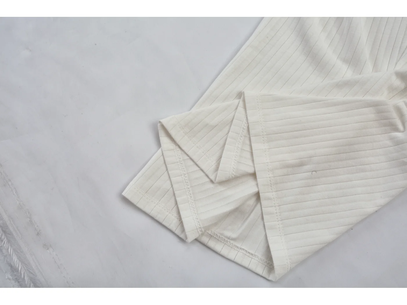 Folded ivory ribbed garments stacked on a plain surface